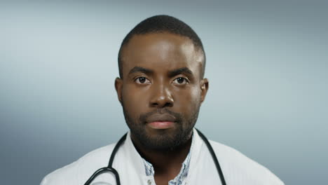Portrait-of-the-young-African-American-good-looking-man-physician-looking-straight-to-the-camera-on-the-grey-wall-background.-Close-up.